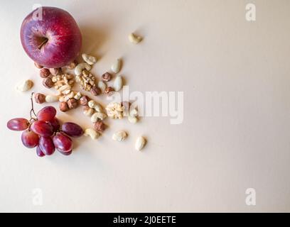 Gesunde natürliche, organische Snacks, verschiedene Nüsse, wie Walnüsse, Cashewkerne, Haselnüsse und Mandeln, Trauben und Äpfel isoliert auf beigem Hintergrund Stockfoto