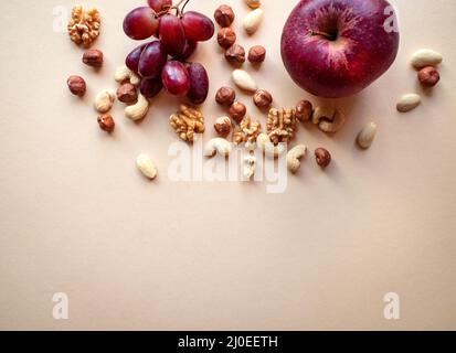 Gesunde natürliche, organische Snacks, verschiedene Nüsse, wie Walnüsse, Cashewkerne, Haselnüsse und Mandeln, Trauben und Äpfel isoliert auf beigem Hintergrund Stockfoto