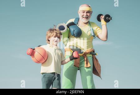 Sportausbildung. Sportsman Großvater und gesundes Kind mit Basketball-Ball auf blauem Himmel Hintergrund. Senior Fitness-Mann und Sohn Training auf blau Stockfoto