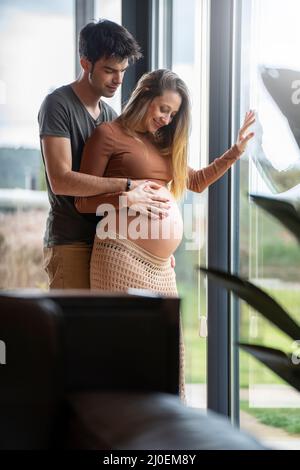 Ein junger Mann umarmte ihre Schwangere am Fenster Stockfoto