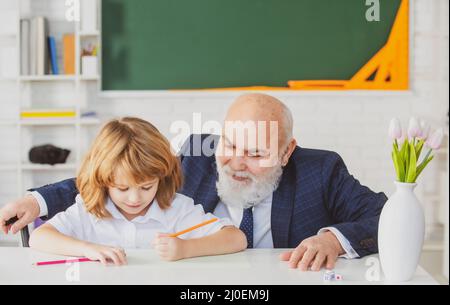 Oberlehrer oder Großvater und Schüler im Klassenzimmer der Schule. Grundschüler lesen und schreiben mit Lehrer im Klassenzimmer. Stockfoto