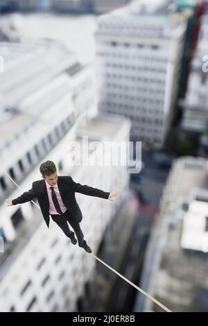 Geschäftsmann, der auf einer Gratwanderung über Gebäude läuft Stockfoto