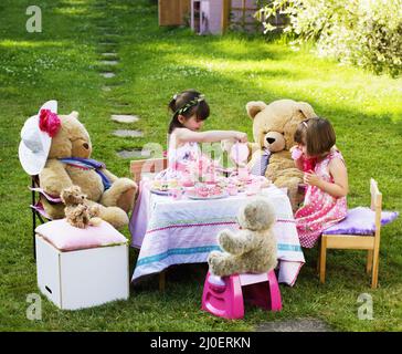 Erhöhter Blick auf zwei junge Mädchen, die in ihrem Garten ein Teddybären-Picknick spielen Stockfoto