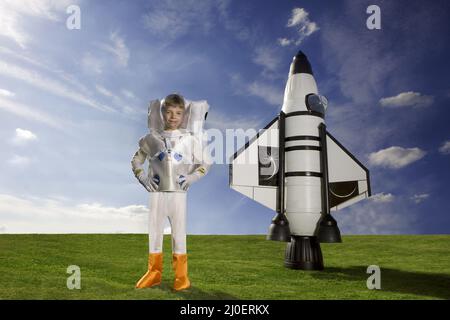 Kleiner kaukasischer Junge, der als Astronaut gekleidet ist und vor seiner Rakete steht.Imagination-Themen dr Stockfoto