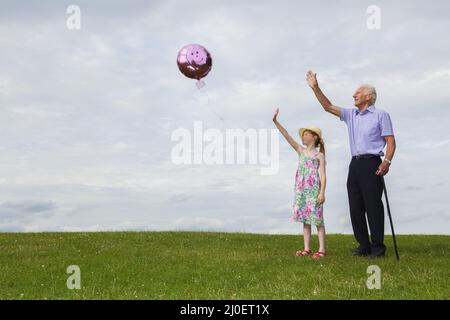 Kaukasische Mädchen und ihr Großvater Freigabe von einem Ballon in den Himmel Stockfoto