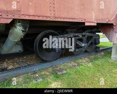Nahaufnahme Sehen Sie sich die schwarzen Räder eines Eisenbahnwagens an, der auf einer Eisenbahnstrecke ruht. Der Schienenwagen ist geparkt und steht für Nostalgie zur Schau. Bokeh. Stockfoto