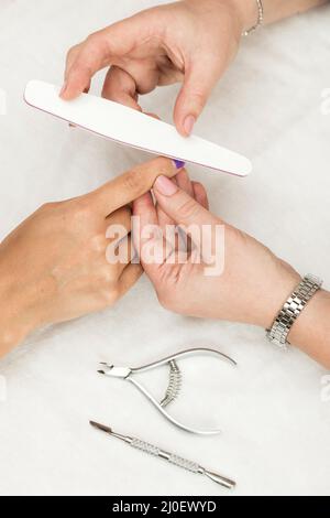 Frau in einem Nagelstudio erhält eine Maniküre von einer Kosmetikerin mit Nagelfeile. Stockfoto