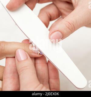 Frau in einem Nagelstudio erhält eine Maniküre von einer Kosmetikerin mit Nagelfeile. Stockfoto