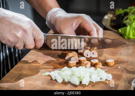 Der Koch schneidet Zwiebeln und Würstchen auf einem Schneidebrett Stockfoto