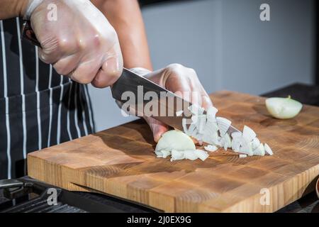 Der Koch schneidet die Zwiebeln auf einem Brett Stockfoto