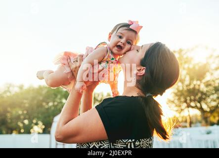 Mollige Wangen, die ich nicht aufhören kann zu küssen. Zugeschnittene Aufnahme einer Mutter, die ihr entzückendes Baby auf der Wange im Hinterhof zu Hause küsst. Stockfoto