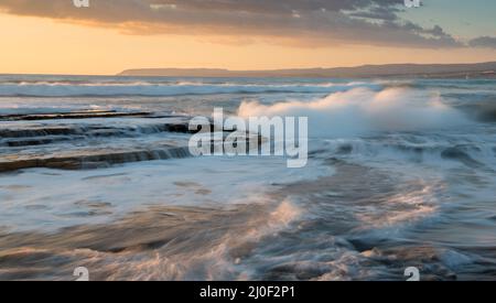 Dramatische, mächtige Wellen, die während des Sonnenuntergangs auf den Meeresfelsen Limassol Cyprus mit der Macht zusammenbrechen Stockfoto