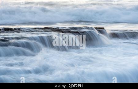 Felsige Küste mit welligem Meer und Wellen, die auf die Felsen krachen Stockfoto