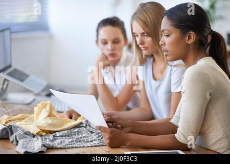 Das perfekte Kleid zu kreieren.... Drei junge Modedesigner diskutieren über ein Design. Stockfoto