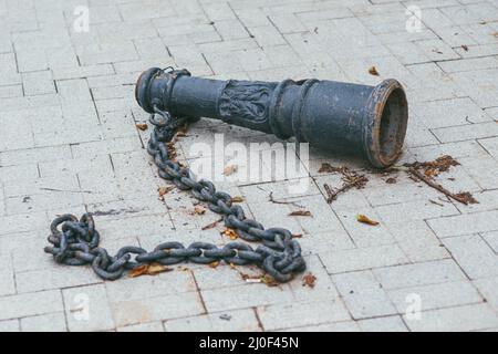 Ein alter antiker rostiger, metallischer Balustrade-Baluster mit einer schweren Kette, die auf einer Fliese in einem Park liegt Stockfoto
