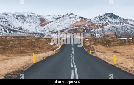 Ländliche leere Straße, die zu den schneebedeckten Bergen in Island führt Stockfoto