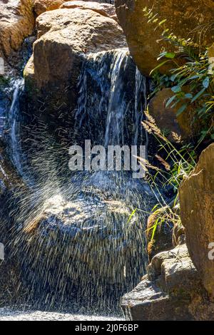 Kleiner Wasserfall, der zwischen Steinen scheint Stockfoto