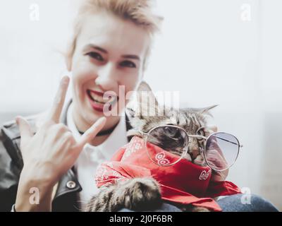 Russland, Sotschi 06.06.2020. Schöne Katze in Sonnenbrille sitzt auf dem Mädchen auf den Rädern und das Mädchen zeigt eine Geste von Rock Stockfoto