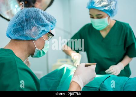 Asian Professional Chirurgen Team Durchführung einer Operation im Operationssaal, Chirurg, Assistentinnen und Krankenschwestern, die Chirurgie an einem Patienten, Gesundheitswagen Stockfoto