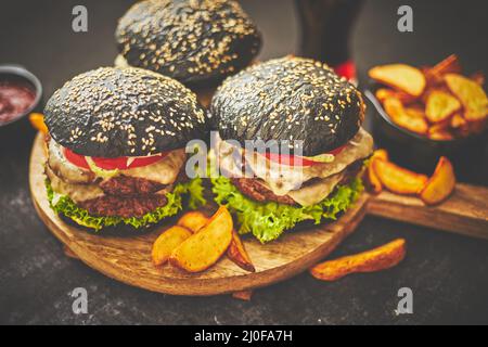 Hausgemachte leckere schwarze Burger serviert auf Holz Schneidebrett mit Ketchup, Kartoffelkeile Stockfoto