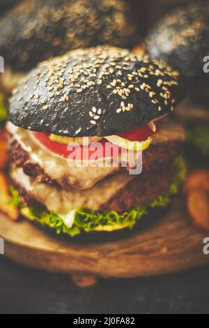 Schwarze doppelte Burger mit Käse. Cheeseburger aus Japan mit schwarzem Brötchen auf dunklem Hintergrund Stockfoto