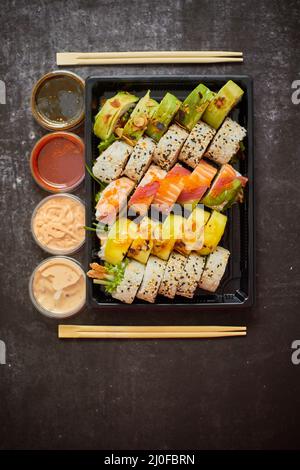 Asiatische Lebensmittel Lieferung nach Hause, verschiedene Sushi-Sets in Kunststoffbehältern mit Saucen, Reis und Essstäbchen Stockfoto