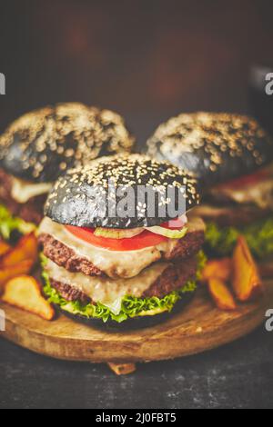 Schwarze doppelte Burger mit Käse. Cheeseburger aus Japan mit schwarzem Brötchen auf dunklem Hintergrund Stockfoto