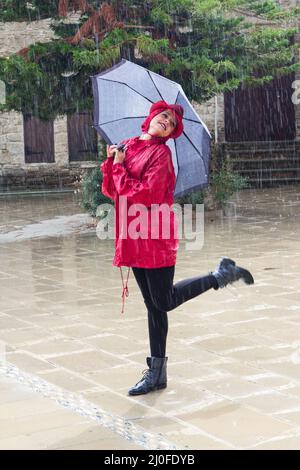 Junge glückliche Frau mit einem Regenschirm, der im Regen tanzt. Stockfoto