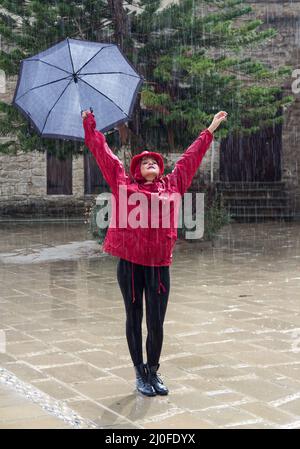 Junge glückliche Frau mit einem Regenschirm, der im Regen tanzt. Stockfoto