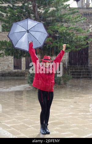 Junge glückliche Frau mit einem Regenschirm, der im Regen tanzt. Stockfoto