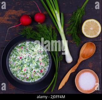 Russische Sommer kalte Suppe Okroshka aus Gemüse, Kvass und Kefir mit Grüns auf dem schwarzen Tisch cl Stockfoto