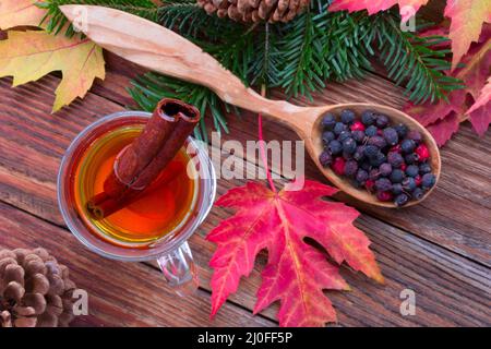 Tee mit Zimt und Zitrone, bunte Herbstblätter von Ahorn, Weißdornbeeren in einem Holzlöffel, ri Stockfoto