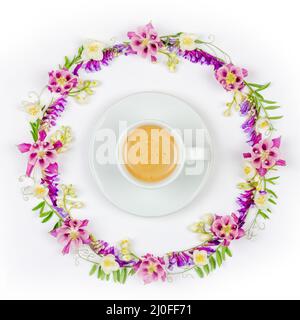 Tasse Kaffee mit Creme in einem runden Vintage floralen Rahmen aus Jasminblüten und Wildblumen auf einem wh Stockfoto