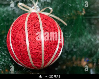 Foto mit Fokus auf einer roten Weihnachtskugel aus Fäden mit goldenem Band auf verschwommenem Hintergrund Stockfoto