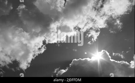 Am Himmel bricht die Sonne durch die Wolken. Schwarzweiß-Foto Stockfoto