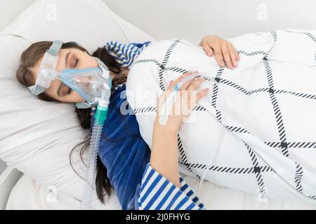 Schwerkranke Jugendliche, die an ein Atemschutzgerät angeschlossen sind, um die Atmung zu unterstützen. COVID-19-Infektion. Stockfoto