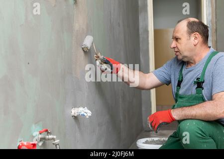 Im Badezimmer trägt ein Bauarbeiter mit einer Walze die Feuchtigkeitsisolierung auf. Stockfoto