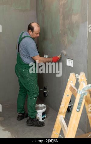 Ein erfahrener Bauarbeiter trägt mit einer Farbwalze eine feuchte Isolierung an die Wand auf. Stockfoto