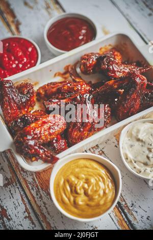 Hähnchenflügel in dicker Grillsauce mit verschiedenen Seiteneinbrüchen. Serviert auf einer weißen gusseisernen Schüssel Stockfoto