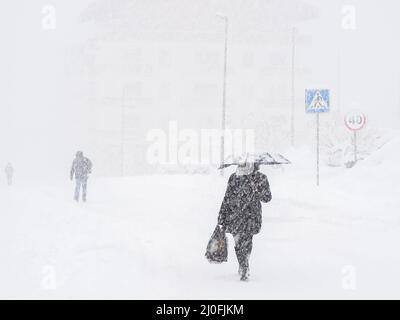 Eine Frau mit einem Sonnenschirm läuft auf einer schneebedeckten Straße Anderen Menschen bei starkem Schneefall folgen Stockfoto