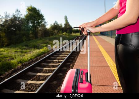 Eine junge Frau legt ihre Hände auf den Griff des Koffers und hält eine Sonnenbrille in der Hand. Reisen Sie mit dem Zug jedes Wochenende oder l Stockfoto