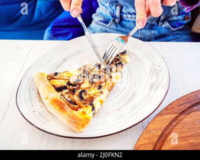 Finger halten eine Gabel und ein Messer, während sie ein schneiden Stück Pilzpizza auf einem Teller liegend Stockfoto