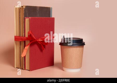 Eine Papptasse Kaffee steht neben einem Stapel alter Bücher, die mit einem roten Band verbunden sind Stockfoto