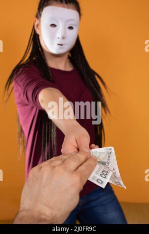 Eine männliche Hand greift nach Papierrechnungen, die von einer anonymen jungen Frau gegeben wurden. Eine isolierte Figur auf einer einfarbigen orangefarbenen Farbe. Stockfoto