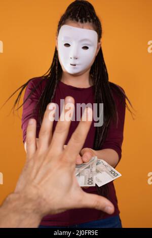 Eine männliche Hand greift nach Papierrechnungen, die von einer anonymen jungen Frau gegeben wurden. Eine isolierte Figur auf einer einfarbigen orangefarbenen Farbe. Stockfoto