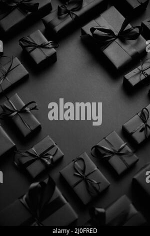 Arrangierte Geschenkschachteln in schwarzem Papier mit schwarzem Band auf schwarzem Hintergrund eingewickelt. Weihnachtskonzept Stockfoto