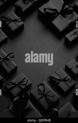 Arrangierte Geschenkschachteln in schwarzem Papier mit schwarzem Band auf schwarzem Hintergrund eingewickelt. Weihnachtskonzept Stockfoto