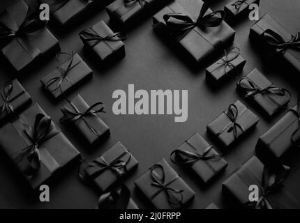 Arrangierte Geschenkschachteln in schwarzem Papier mit schwarzem Band auf schwarzem Hintergrund eingewickelt. Weihnachtskonzept Stockfoto