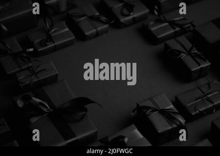 Arrangierte Geschenkschachteln in schwarzem Papier mit schwarzem Band auf schwarzem Hintergrund eingewickelt. Weihnachtskonzept Stockfoto