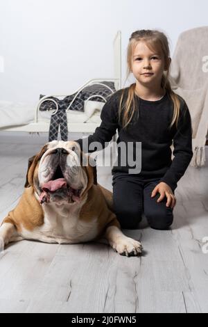 Das Mädchen sitzt auf dem Boden neben dem Gürtel der englischen Bulldogge und streichelt ihn sanft mit ihrer Hand. Mann und Hund. Stockfoto